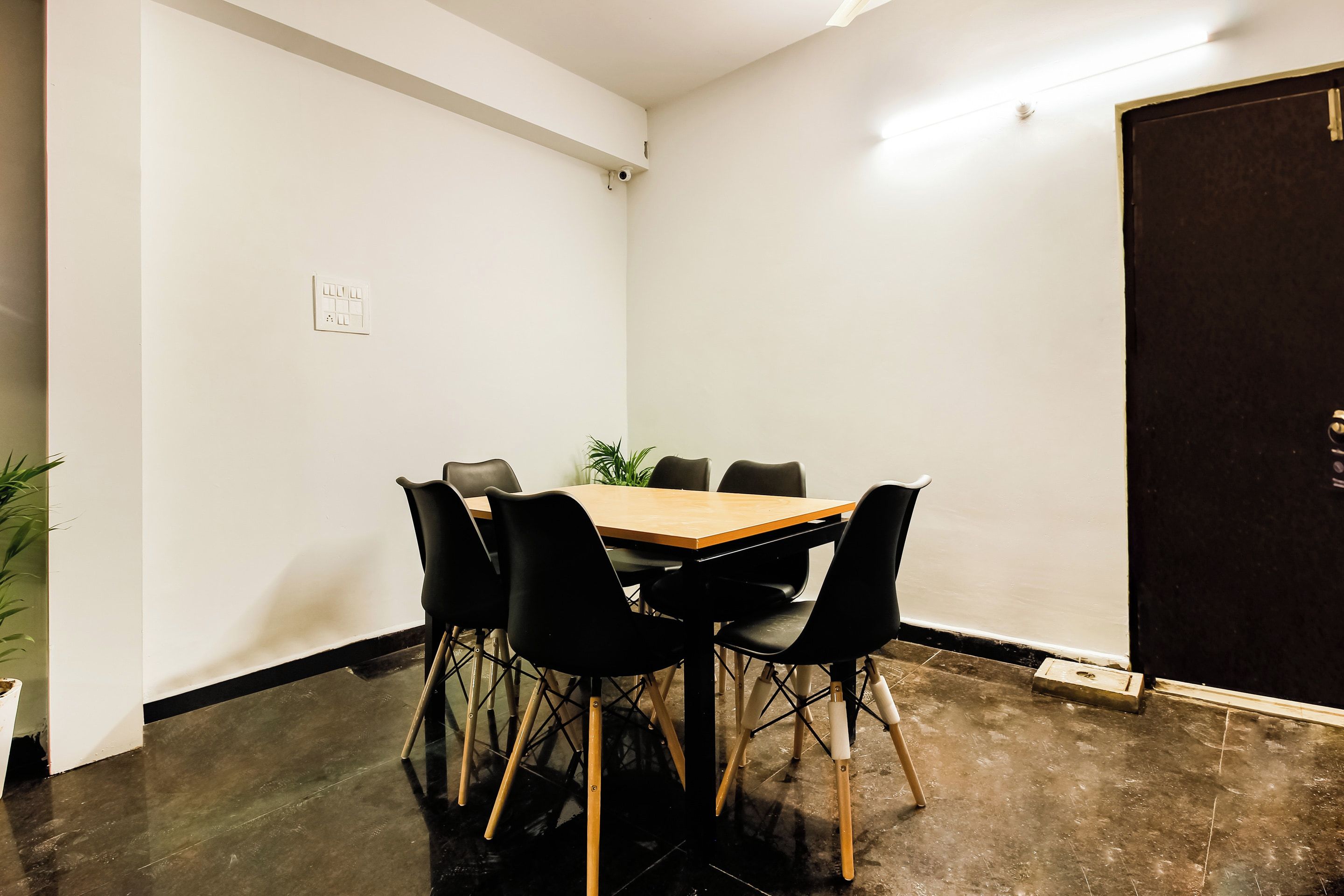Uma sala de conferências com mesa de madeira, cadeiras pretas e um vaso de planta.