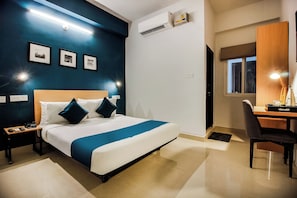 A hotel room with a bed, bedside tables, a desk, a chair, a window, and wall-mounted air conditioning. - Hotel O GACHIBOWLI BESIDE DLF  (Hyderabad)