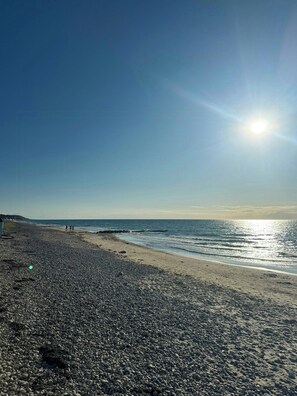 A pebbled beach with a clear sky and the sun shining. - Holiday home with enclosed garden and terrace (Græsted)