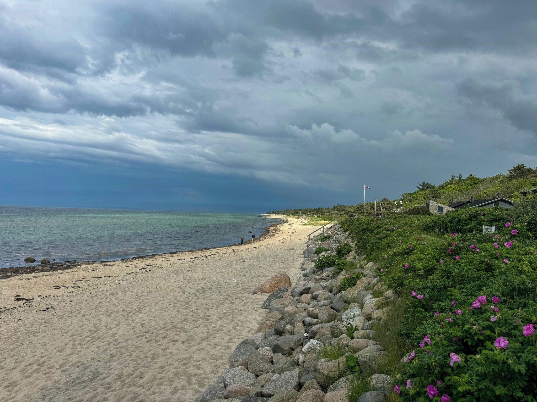 A beach with a rocky shoreline, a clear view of the ocean, and a cloudy sky.
