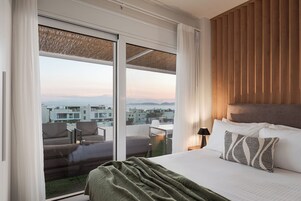 Habitación de hotel con una cama grande, vistas a la ciudad y un balcón con mobiliario.