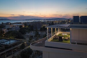 Un edificio moderno con terraza en la azotea y vistas a un paisaje urbano al anochecer.