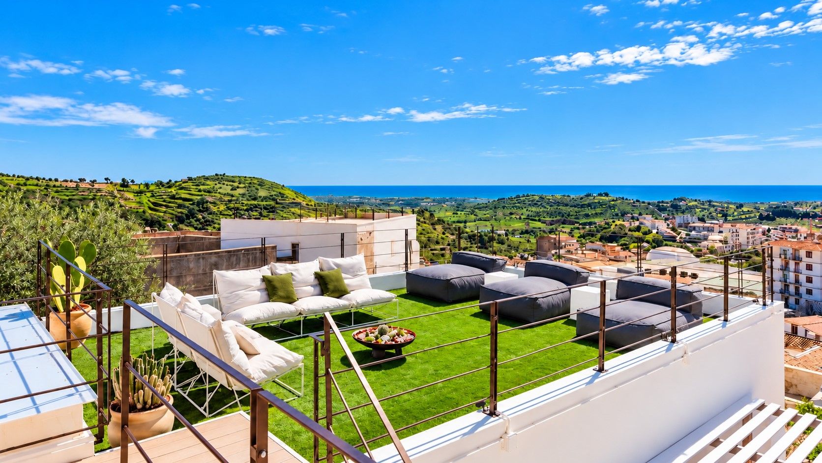 Eine Dachterrasse mit Sitzgelegenheiten im Freien, einem kleinen Tisch und Blick auf das Meer und die umliegende Landschaft.