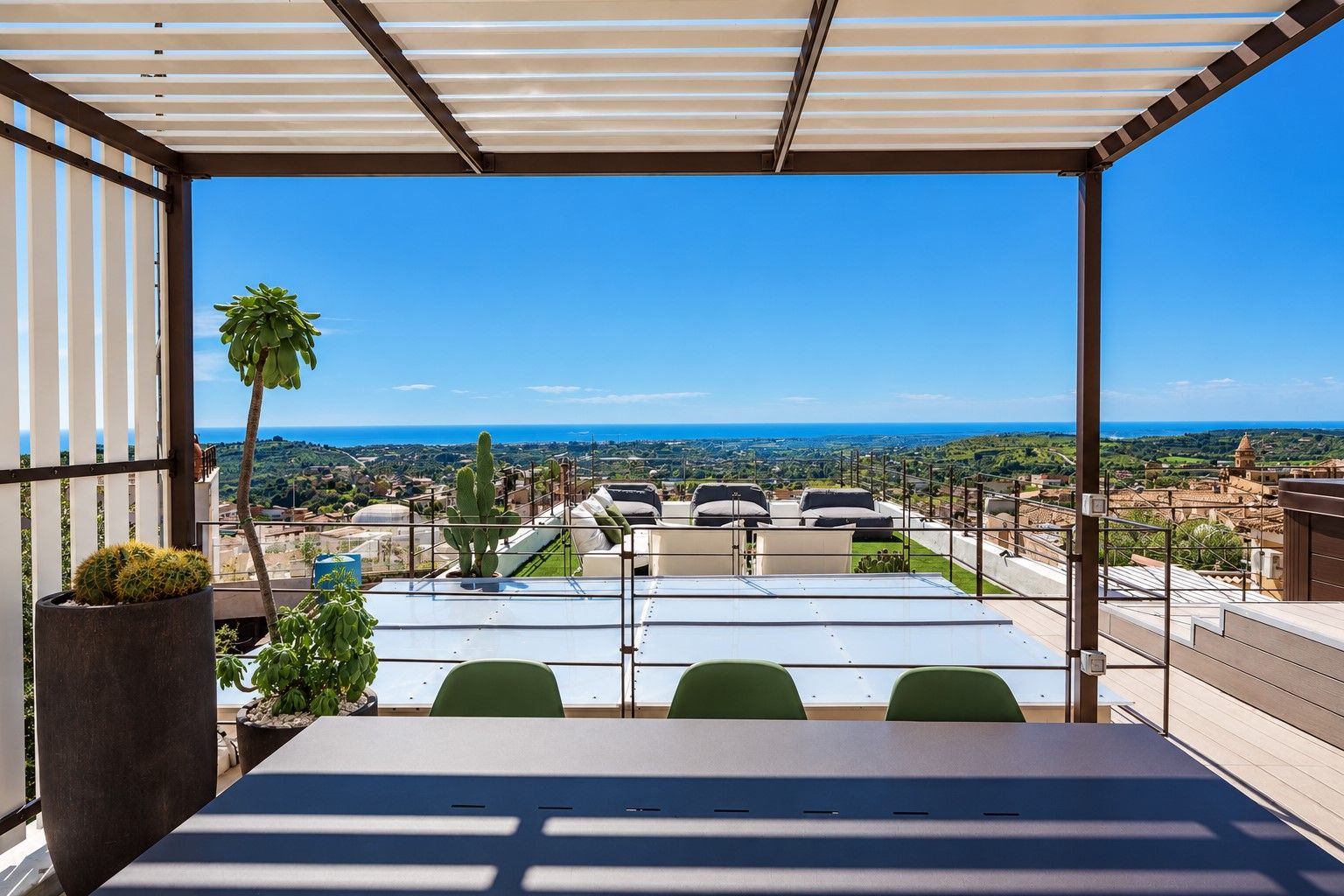Eine Terrasse mit Tisch und Stühlen, einer Kakteenpflanze und Blick auf Stadt und Küste.