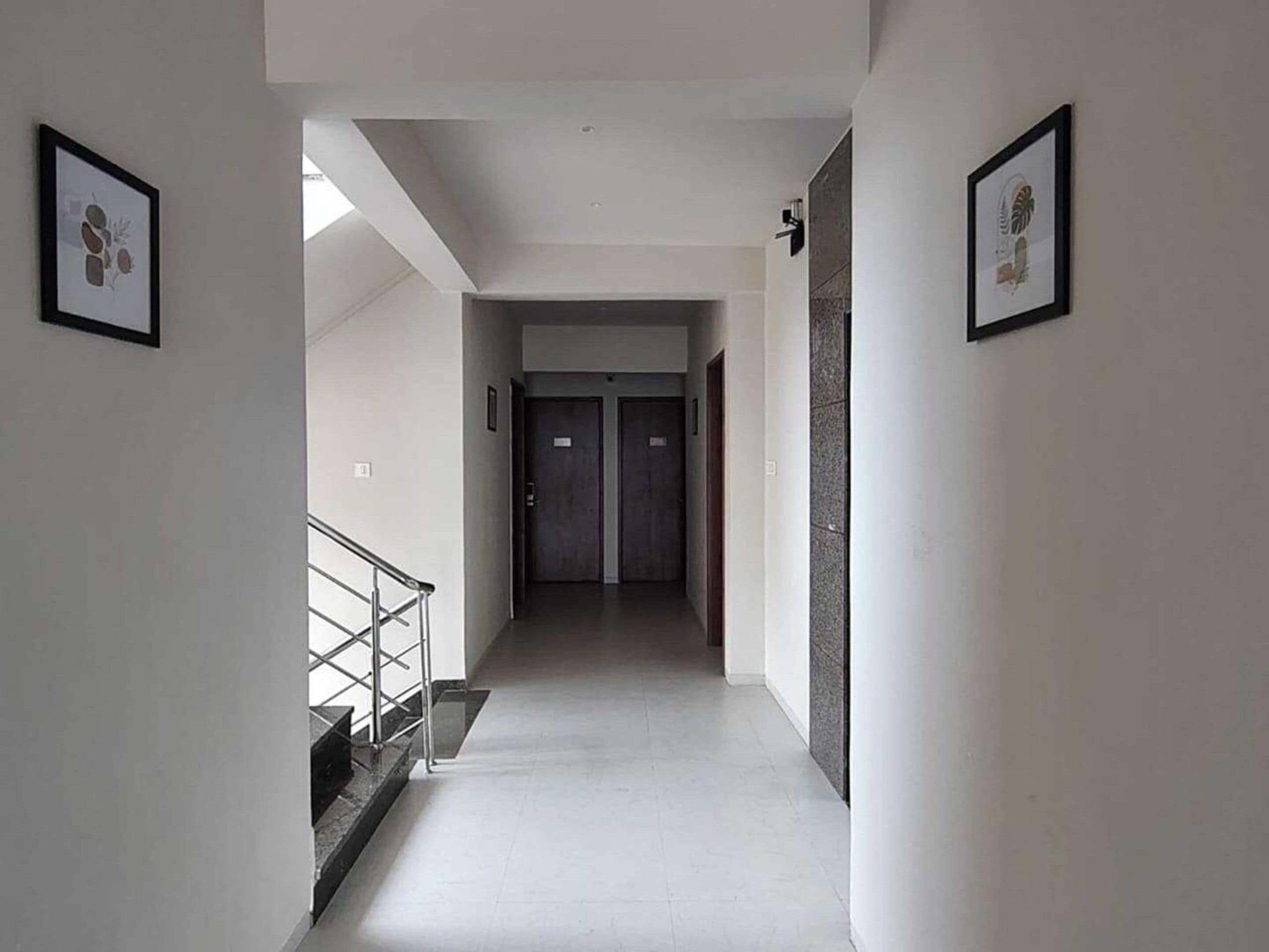 A hallway with a staircase on the left, two doors at the end, and framed pictures on the walls.