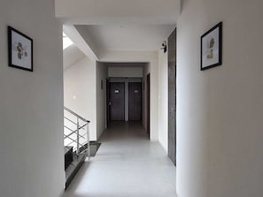 A hallway with a staircase on the left, two doors at the end, and framed pictures on the walls. - Classic Nilay Inn (Pandharpur)