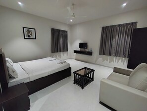 A modern hotel room with a bed, a sofa, a small table, a TV, and curtains. - Classic Nilay Inn (Pandharpur)