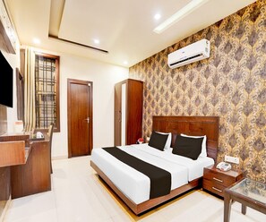 A hotel room with a large bed, a desk with a telephone, and an air conditioning unit on the wall. - Classic Hotel Nirmal Residency (Bhopal)