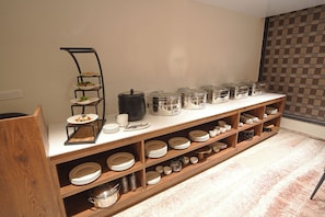 A buffet setup with multiple serving stations, including a salad bar, hot food containers, and a variety of plates and bowls.