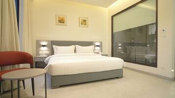 Habitación de hotel con cama, mesitas de noche, una silla, una pequeña mesa y un ventanal grande.