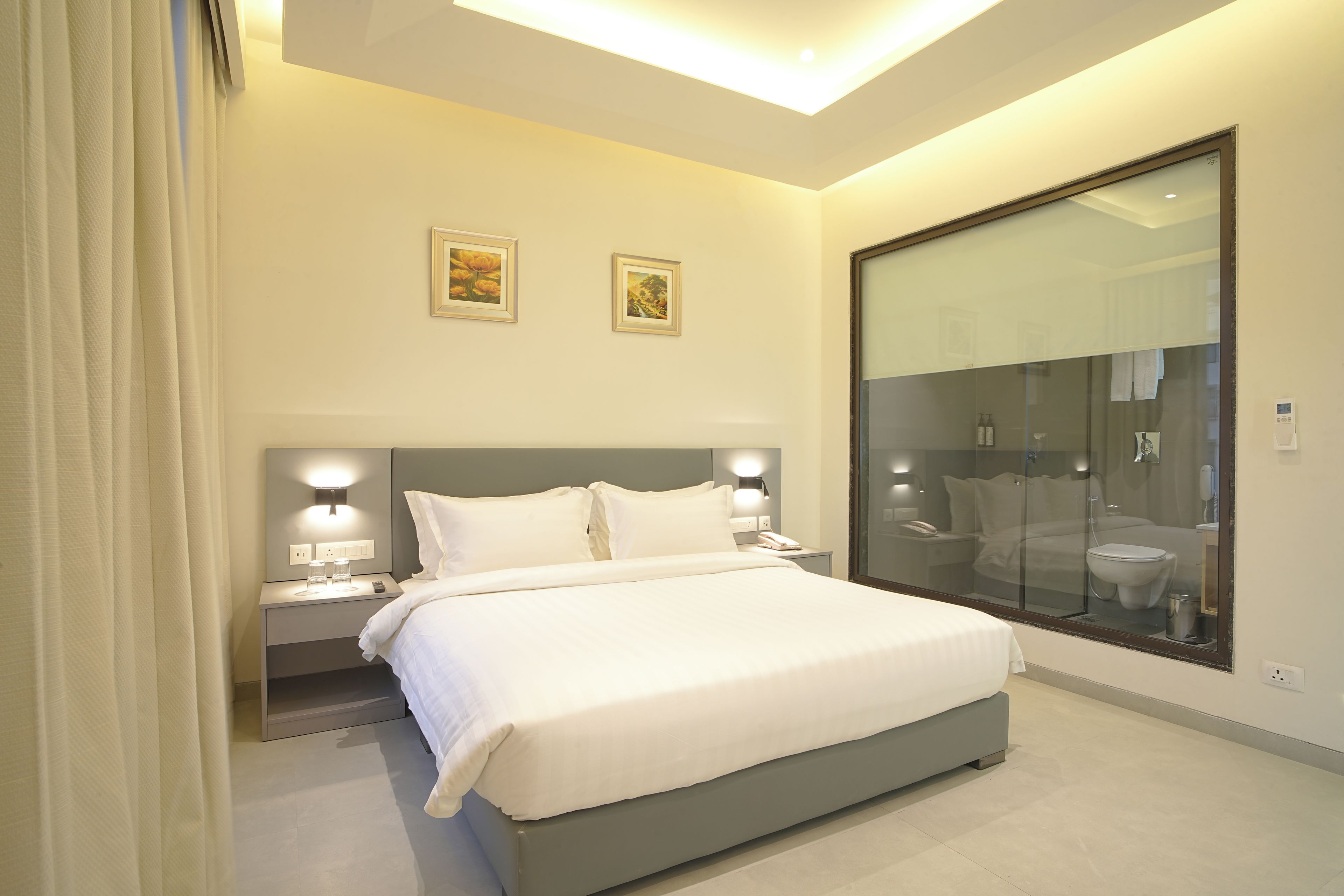Una habitación de hotel moderna con una cama grande, lámparas de noche, una mesita de noche y un box de ducha de vidrio.