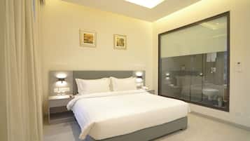 Una habitación de hotel moderna con una cama grande, lámparas de noche, una mesita de noche y un box de ducha de vidrio.