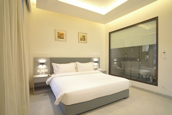 Una habitación de hotel moderna con una cama grande, lámparas de noche, una mesita de noche y un box de ducha de vidrio.
