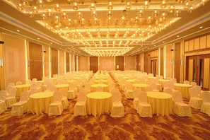 A banquet hall with round tables and chairs, a patterned carpet, and a ceiling with hanging spherical lights.
