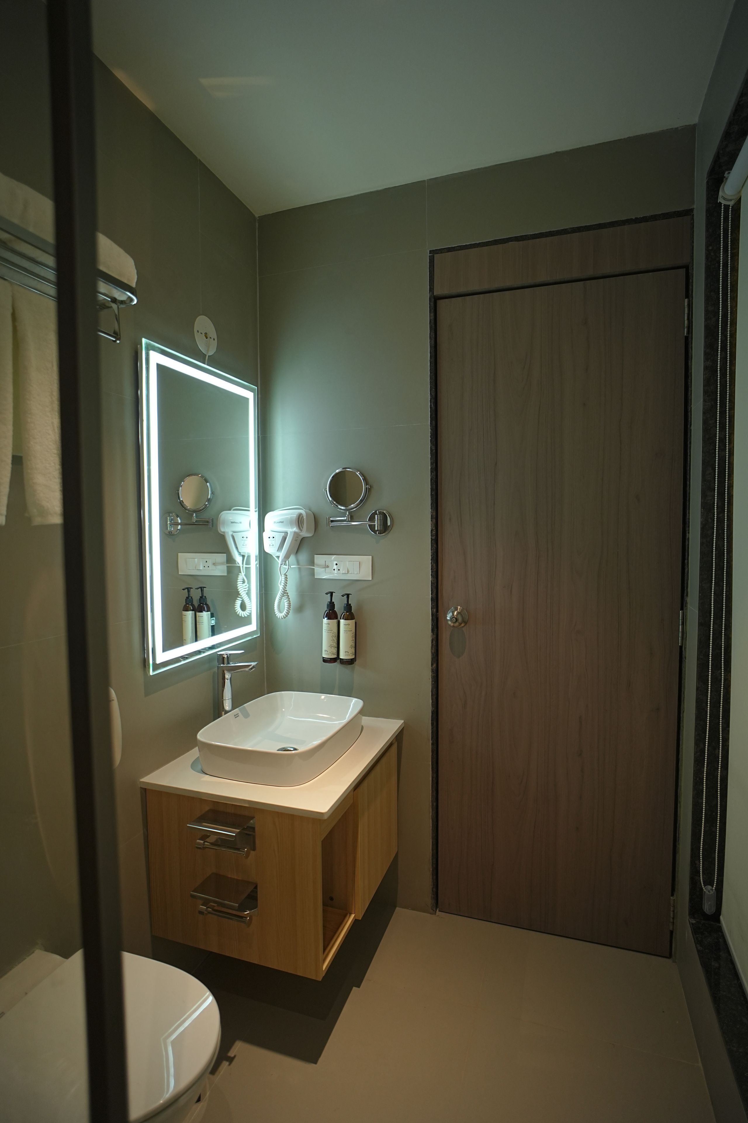 Un baño con un lavabo blanco, un espejo, un secador de pelo y una puerta de madera.
