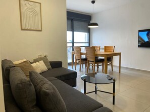 A modern living room with a sectional sofa, a glass coffee table, and a dining area with wooden chairs and a table. - Mesilat Yesharim Penthouse  (Jerusalem)