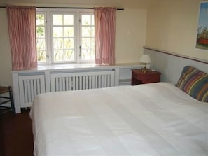 Une chambre à coucher avec un lit, une table de chevet, une fenêtre avec des rideaux et un radiateur.
