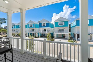 A covered outdoor area with a wooden deck, white railings, and a view of a row of blue and white buildings with balconies. - The Blue Seeker Steps to Beach Pet Friendly (Myrtle Beach)