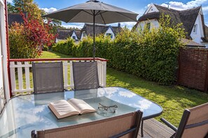 An outdoor patio with a glass table, two chairs, an open book, and a pair of glasses. - Wellenläufer Vacation Home in Glowe – Sauna, Fireplace & Baltic Sea Vacation (Glowe)
