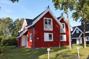 A red two-story house with white trim, a front porch, and satellite dishes on the roof. - Wellenläufer Vacation Home in Glowe – Sauna, Fireplace & Baltic Sea Vacation (Glowe)