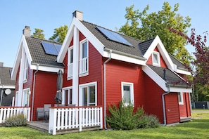 Ein rotes Haus mit Solaranlage, einer weißen Veranda und einem kleinen Garten.