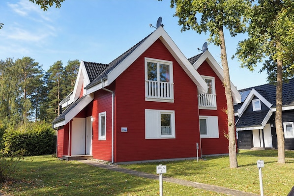 Ein rotes, zweistöckiges Haus mit weißer Tür, Fenstern und einem kleinen Balkon.