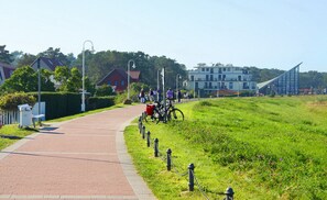 A paved pathway with a grassy area on one side, a row of bollards, and a building in the background. - Wellenläufer Vacation Home in Glowe – Sauna, Fireplace & Baltic Sea Vacation (Glowe)