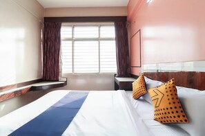 Een hotelkamer met een bed, een raam met gordijnen, een nachtkastje en een aan de muur bevestigde televisie.