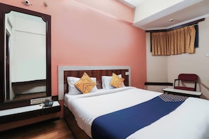 Habitación de hotel con cama, escritorio, silla, espejo y ventana con cortinas.