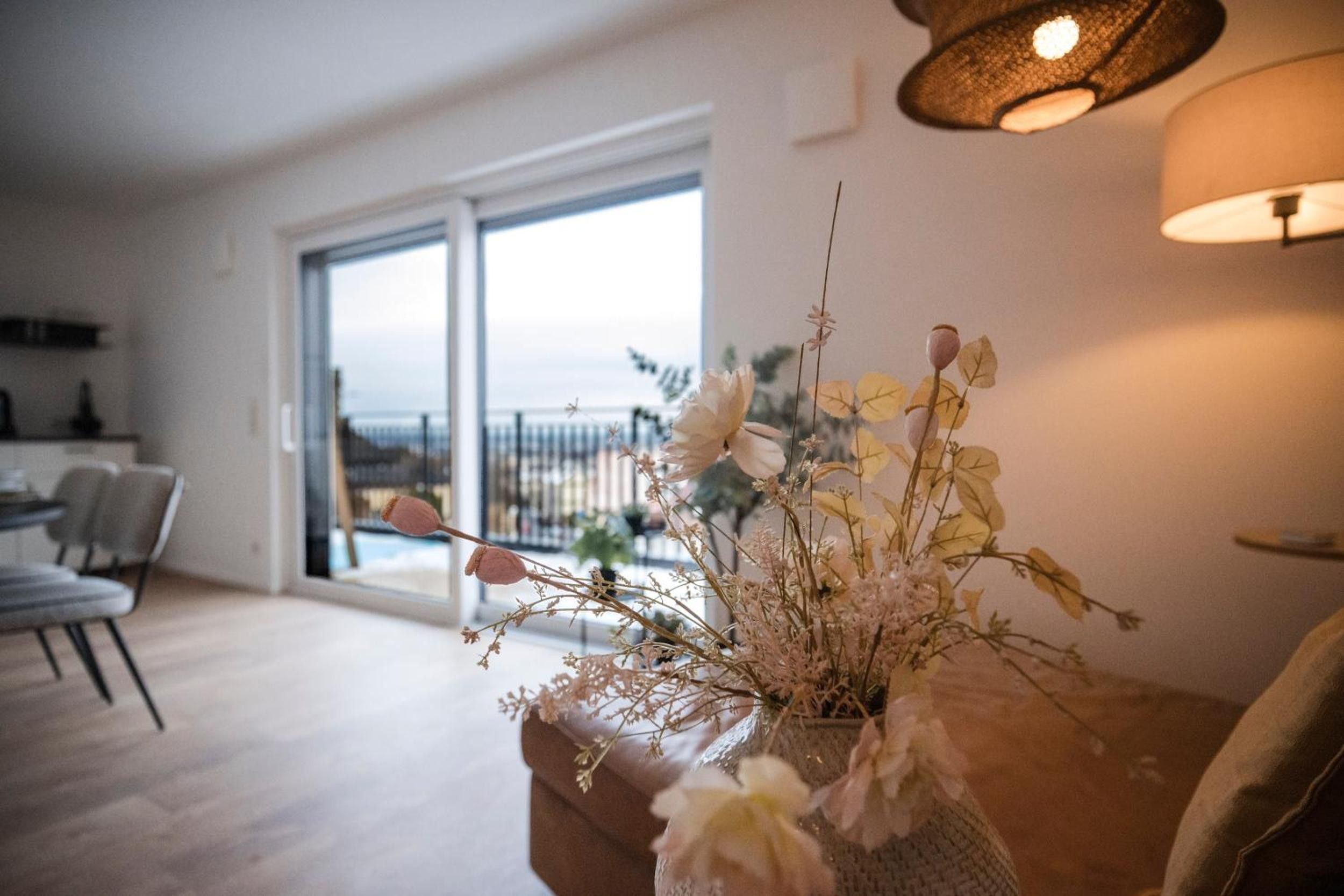 Ein Wohnzimmer mit großem Fenster, einer Couch und einer Vase mit getrockneten Blumen.