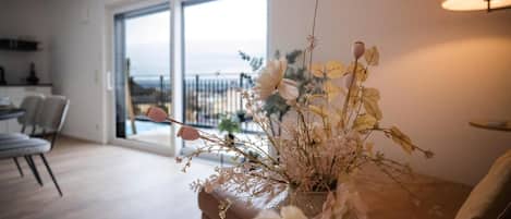 A living room with a large window, a sofa, and a vase with dried flowers.