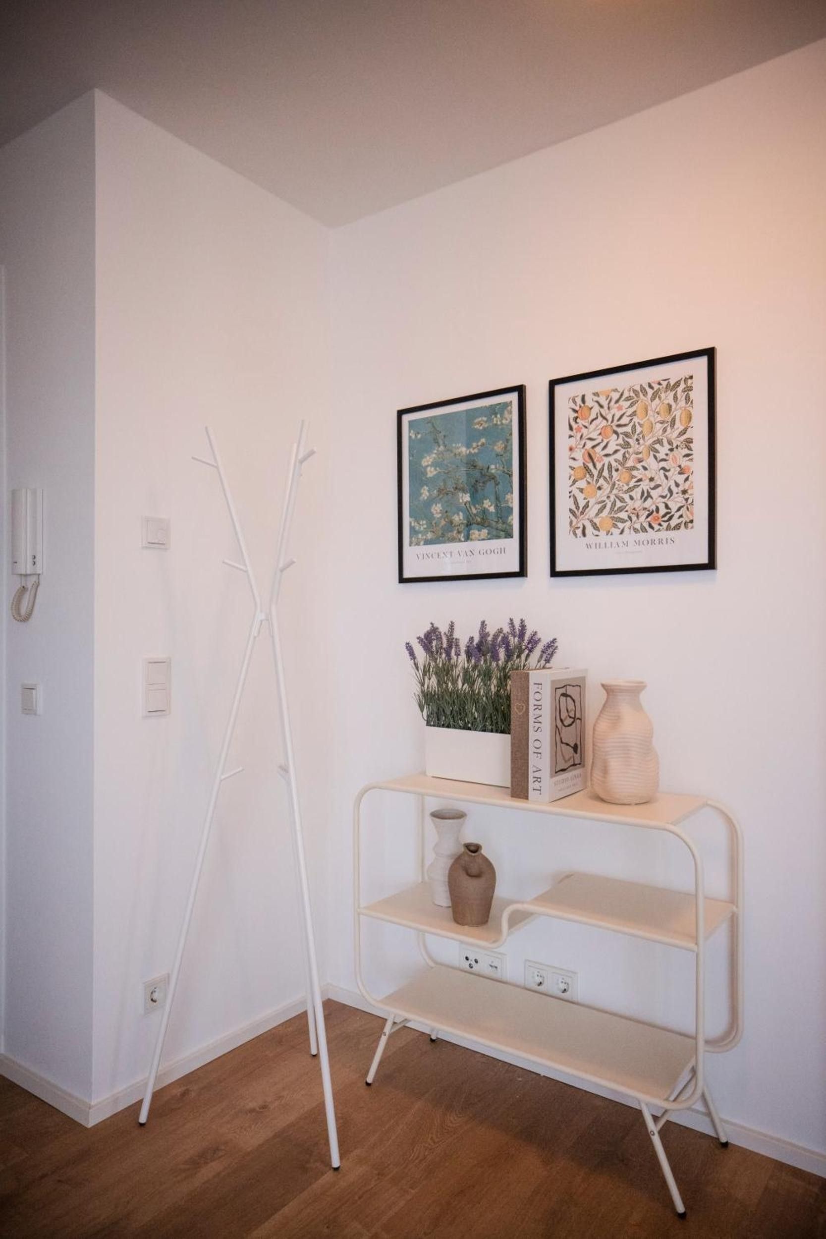 A minimalist room with a white wall, a white metal shelf, and two framed artworks.