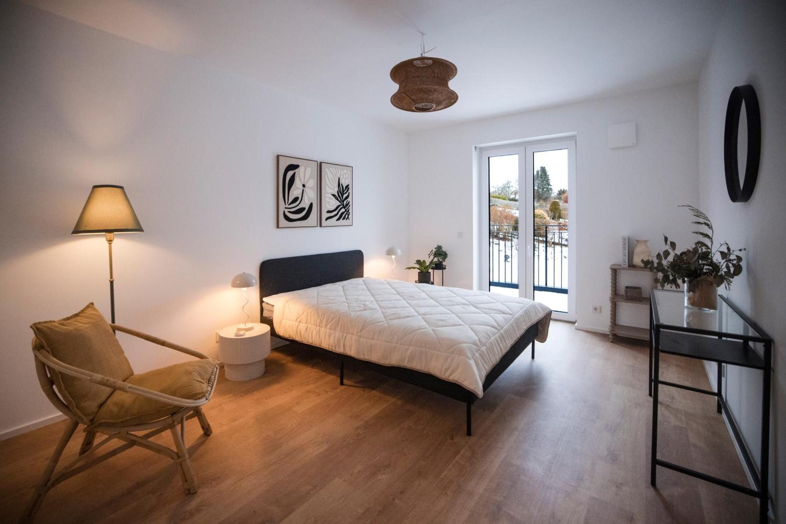 Ein Schlafzimmer mit Bett, Stuhl, Lampe und Blick ins Freie durch eine Tür.
