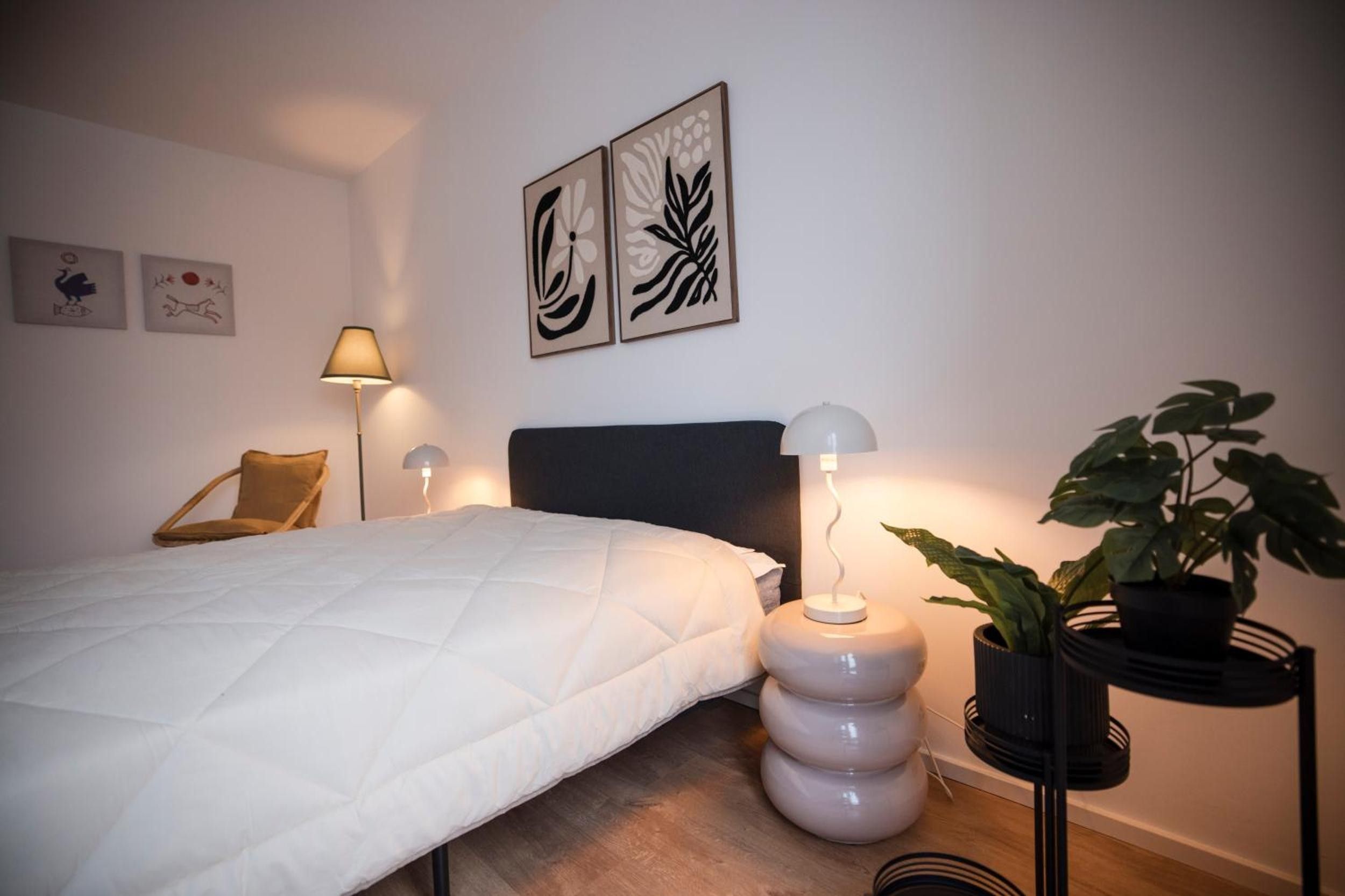 A bedroom with a bed, two wall-mounted lamps, a chair, and a potted plant.