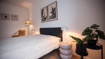 A bedroom with a bed, two wall-mounted lamps, a chair, and a potted plant.