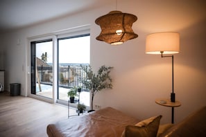 Ein modernes Wohnzimmer mit einer Couch, einer Lampe und Blick auf einen Balkon mit Pflanzen.