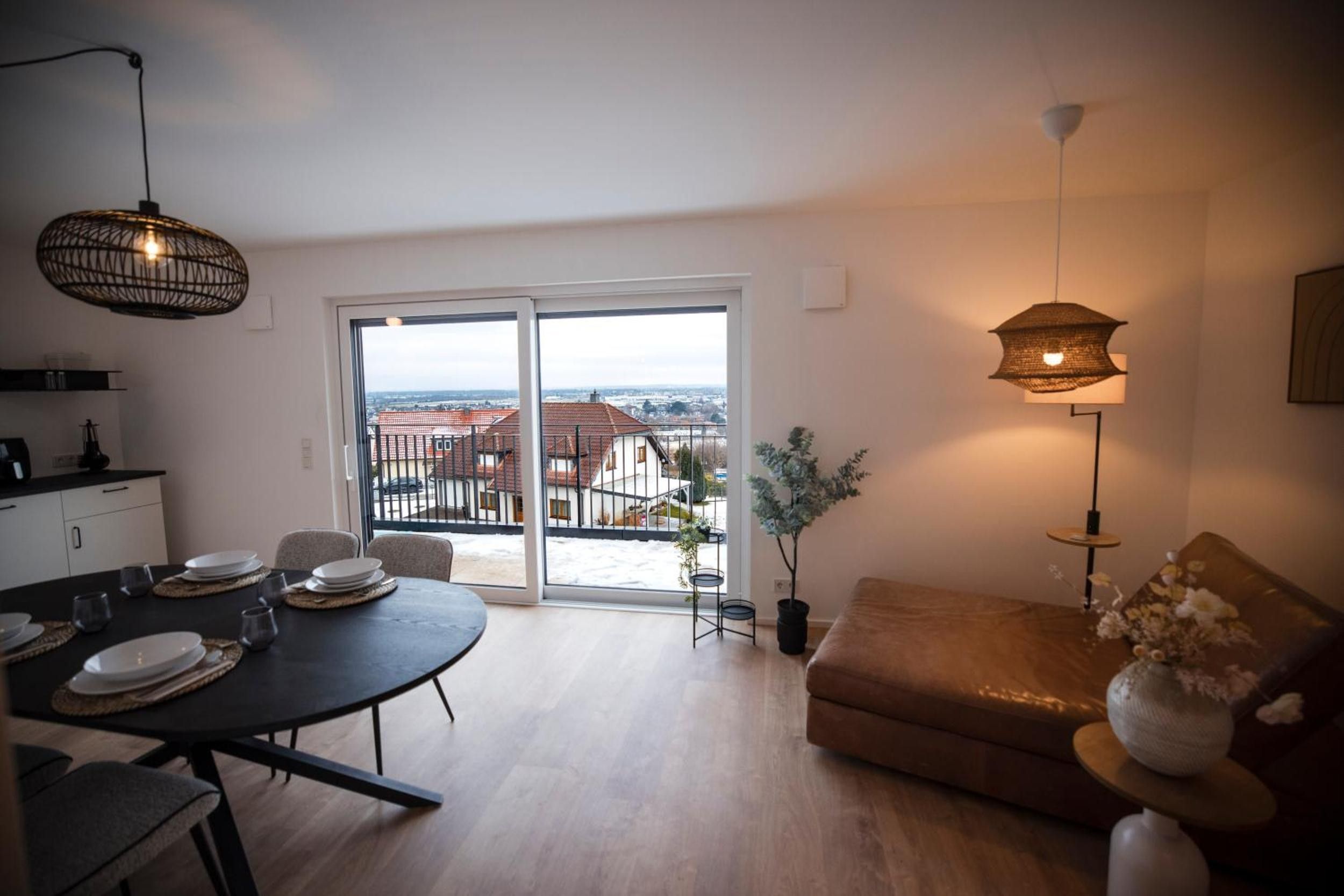 Ein modernes Wohnzimmer mit Essbereich, einer Couch, einer Zimmerpflanze und Blick durch die Glastür.