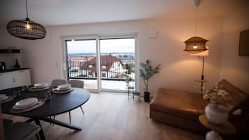 Ein modernes Wohnzimmer mit Essbereich, einer Couch, einer Zimmerpflanze und Blick durch die Glastür.
