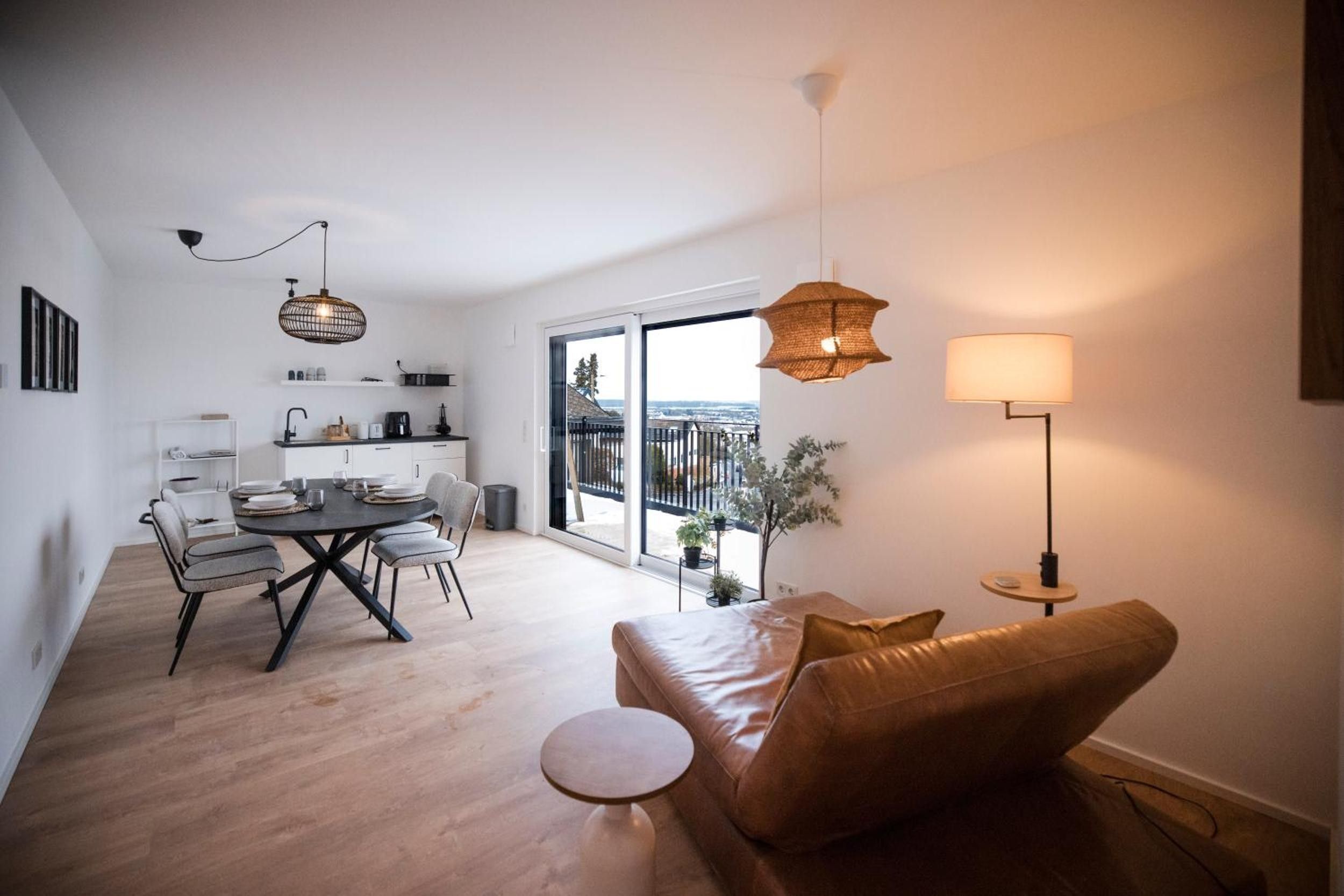 A modern living space with a dining area, a sofa, a coffee table, and a balcony with a view.
