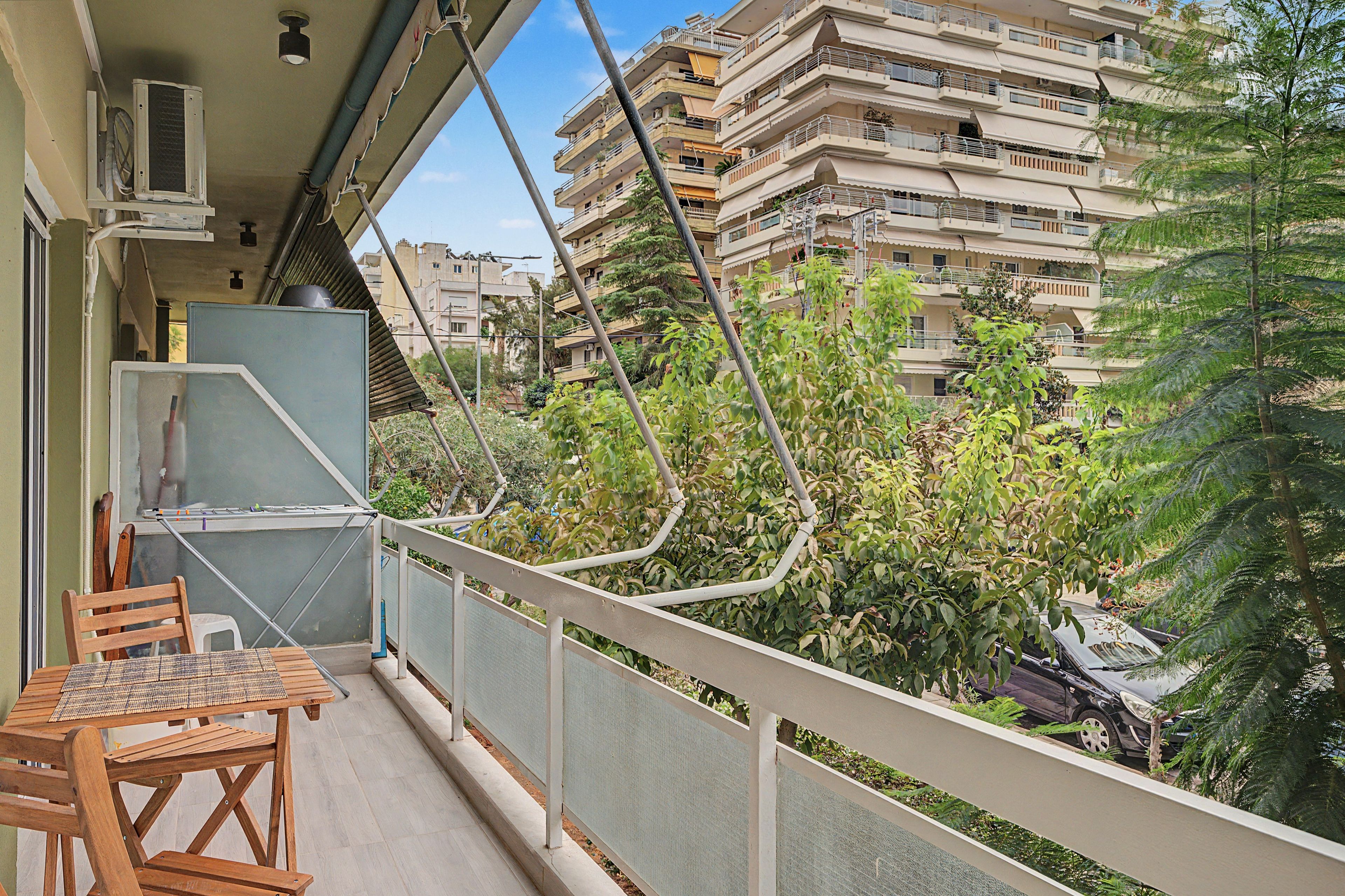 A balcony with a table and chairs, overlooking a residential area with multi-story buildings and greenery.