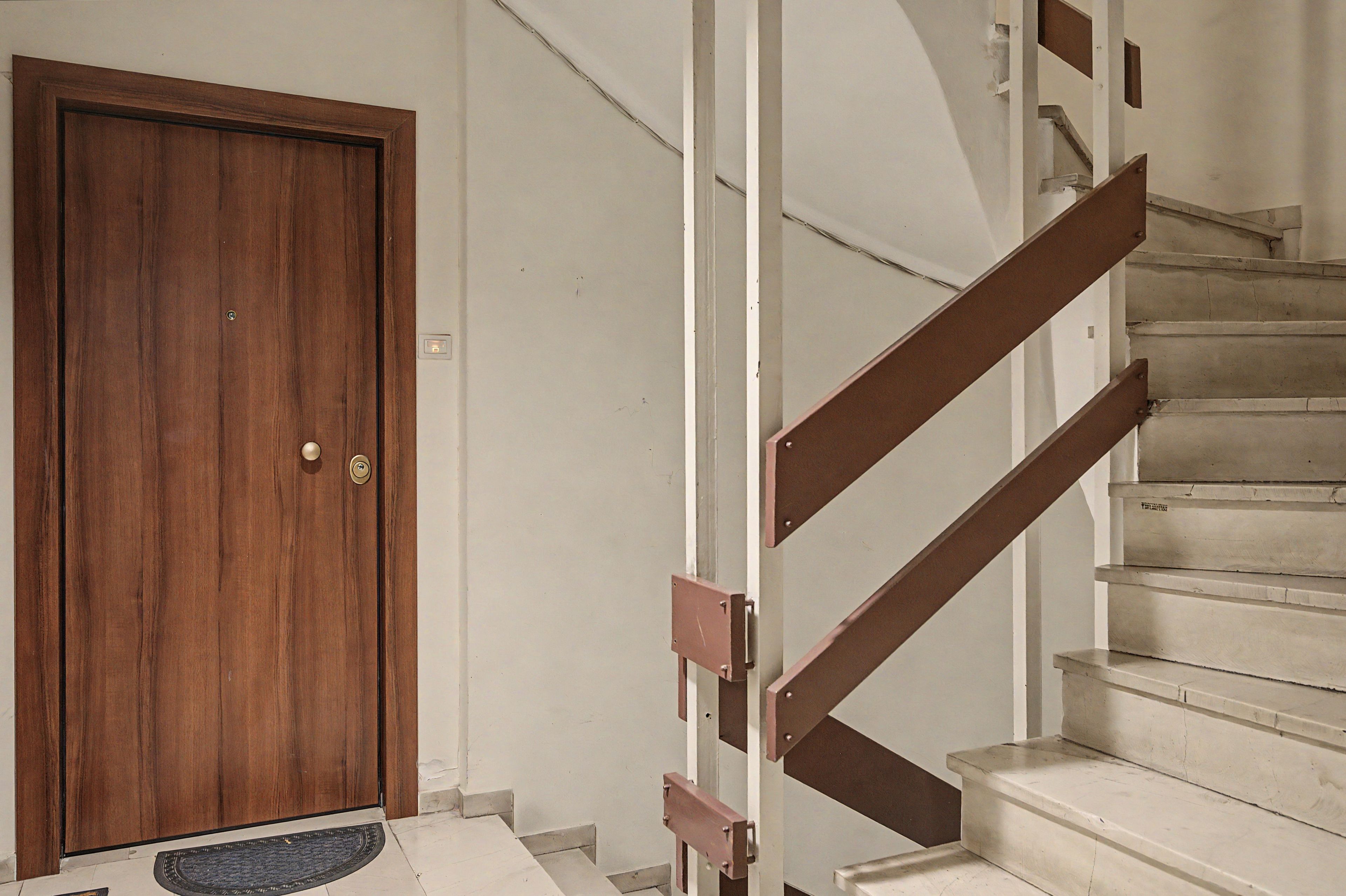 A wooden door with a doormat, a staircase with wooden handrails, and a white wall.