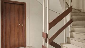 A wooden door with a doormat, a staircase with wooden handrails, and a white wall.