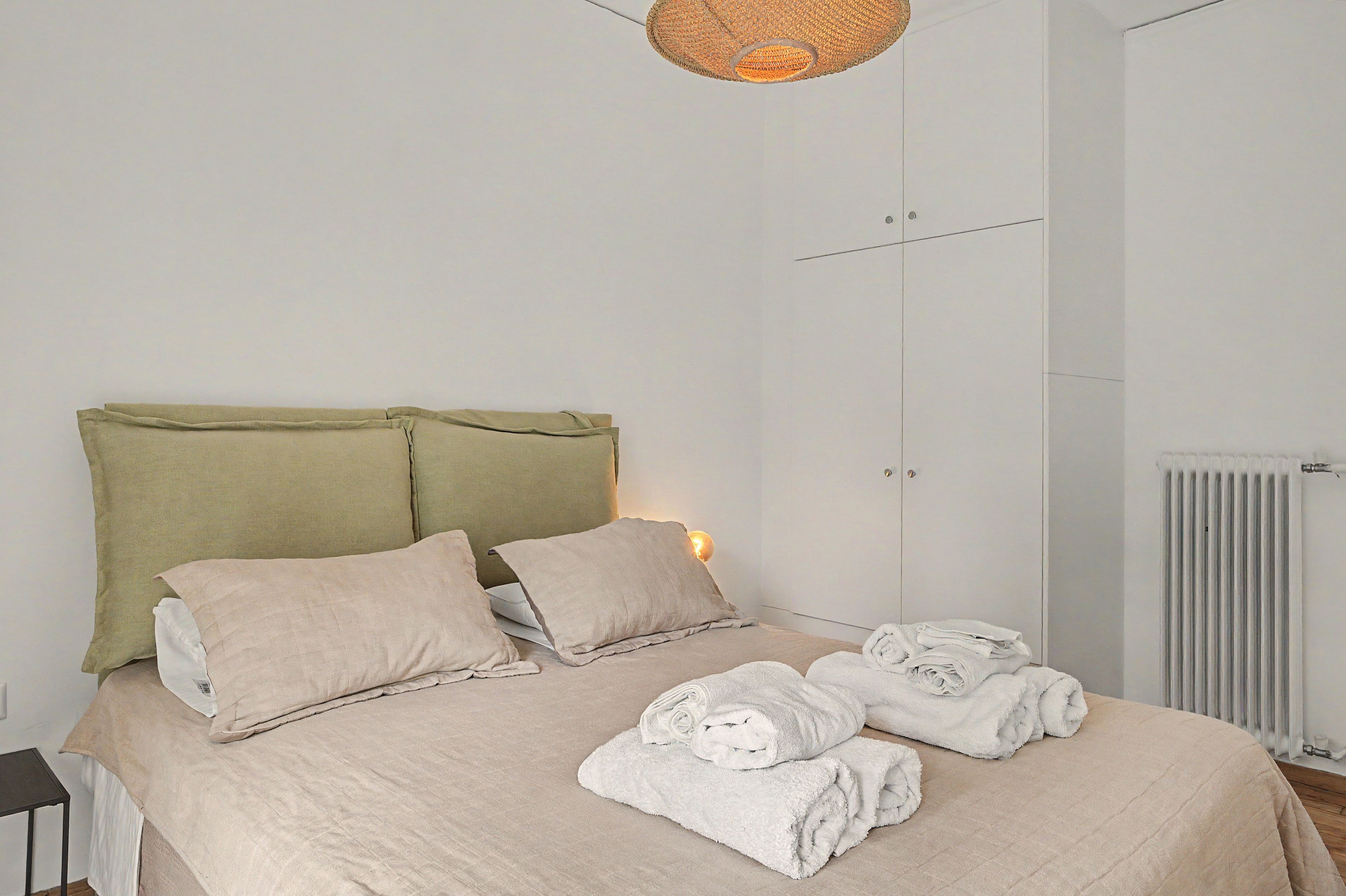 A bed with a headboard, pillows, and rolled towels.