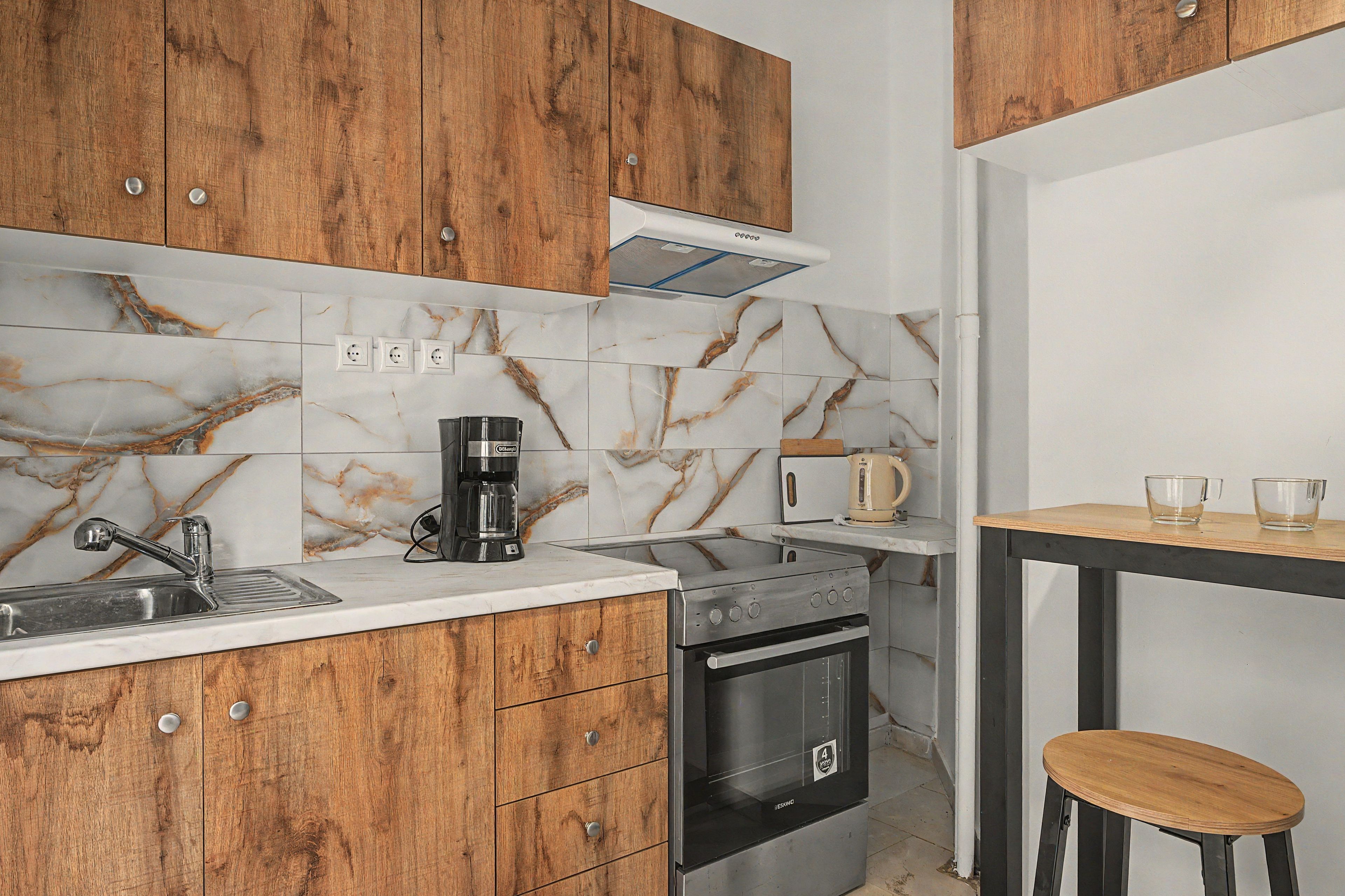 A kitchen with wooden cabinets, a stainless steel sink, a coffee maker, a toaster, and a small wooden table with two cups.