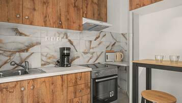 A kitchen with wooden cabinets, a stainless steel sink, a coffee maker, a toaster, and a small wooden table with two cups.
