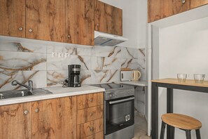 Una cocina con armarios de madera, un lavamanos de acero inoxidable, una cafetera, un tostador y una pequeña mesa de madera con dos tazas.