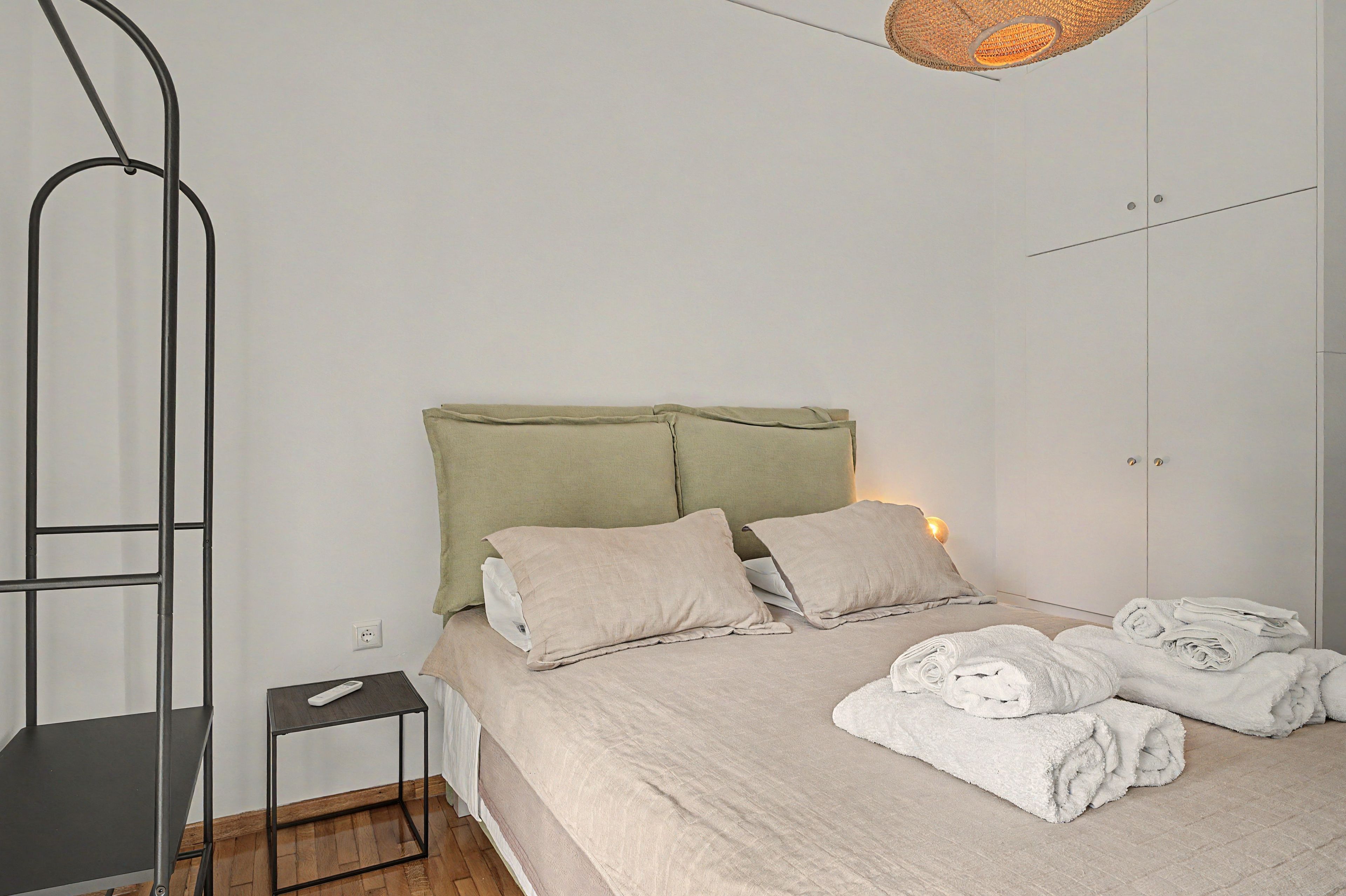 A bedroom with a bed, pillows, a bedside table, a hanging light fixture, and a folded towel on the floor.
