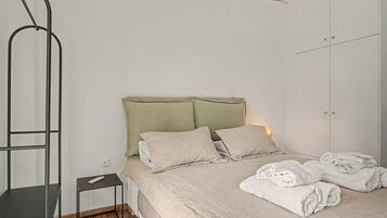 A bedroom with a bed, pillows, a bedside table, a hanging light fixture, and a folded towel on the floor.