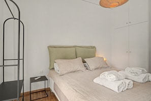 Un dormitorio con una cama, almohadas, una mesita de noche, una lámpara colgante y una toalla doblada en el suelo.