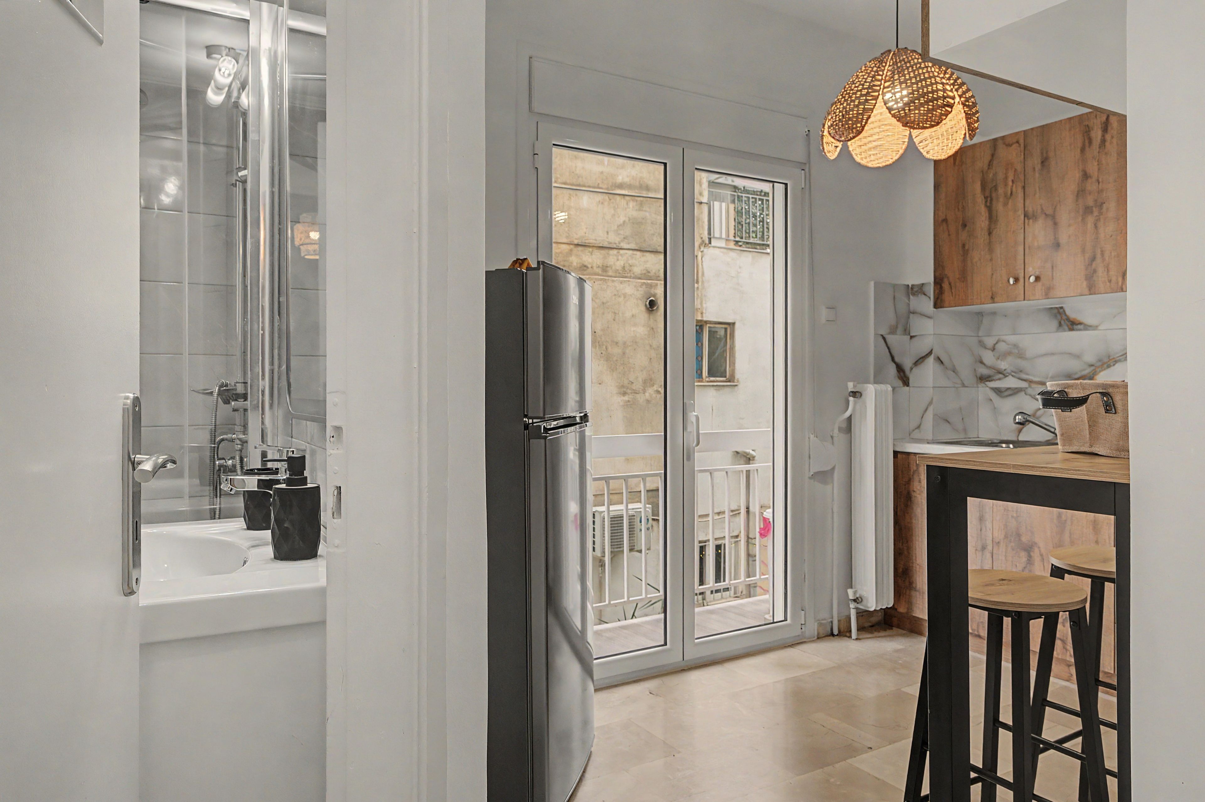 A modern kitchen with a refrigerator, a sink, and a dining area with stools.